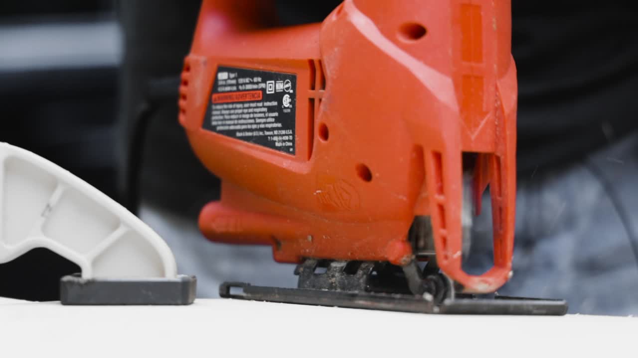 primer plano de una sierra de calar eléctrica naranja que atraviesa un trozo de madera, herramienta eléctrica
