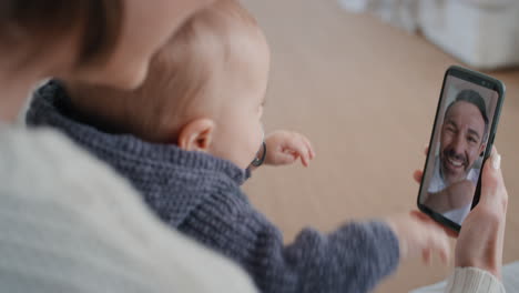 Madre-Y-Bebé-Usando-Un-Teléfono-Inteligente-Conversando-Por-Video-Con-El-Padre-Saludando-Al-Bebé-En-La-Pantalla-Disfrutando-Comunicándose-Con-La-Familia-A-Través-De-Una-Conexión-De-Teléfono-Móvil-4k