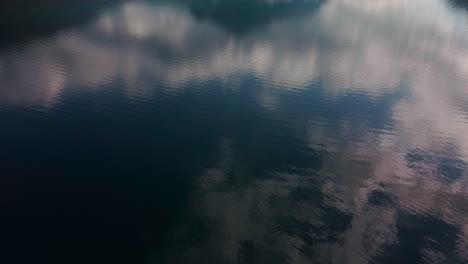 Slow-tilting-movement-flying-over-the-Thunersee-lake,-revealing-the-beautiful-mountain-landscape,-reflected-in-the-blue-surface-of-the-lake