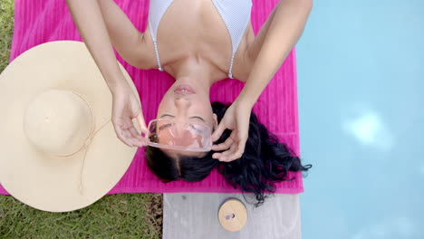 Relaxing by pool, woman in sunglasses lying on pink towel