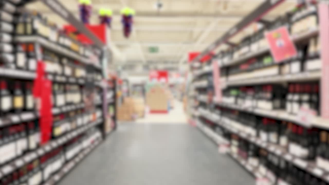 Out of focus tracking shot travels down a retail store aisle lined with wine bottles