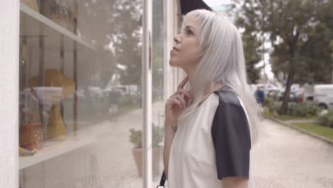 pensive female shopaholic staring and pointing at shop window