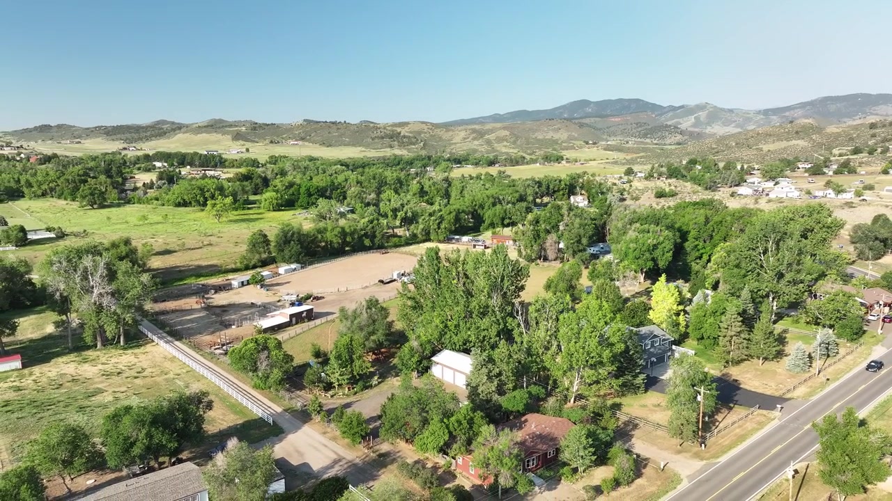 Ripresa dall'alto che si affaccia su un grande fienile bianco e una tenuta rurale annidata vicino alle colline pedemontane della Front Range del Colorado