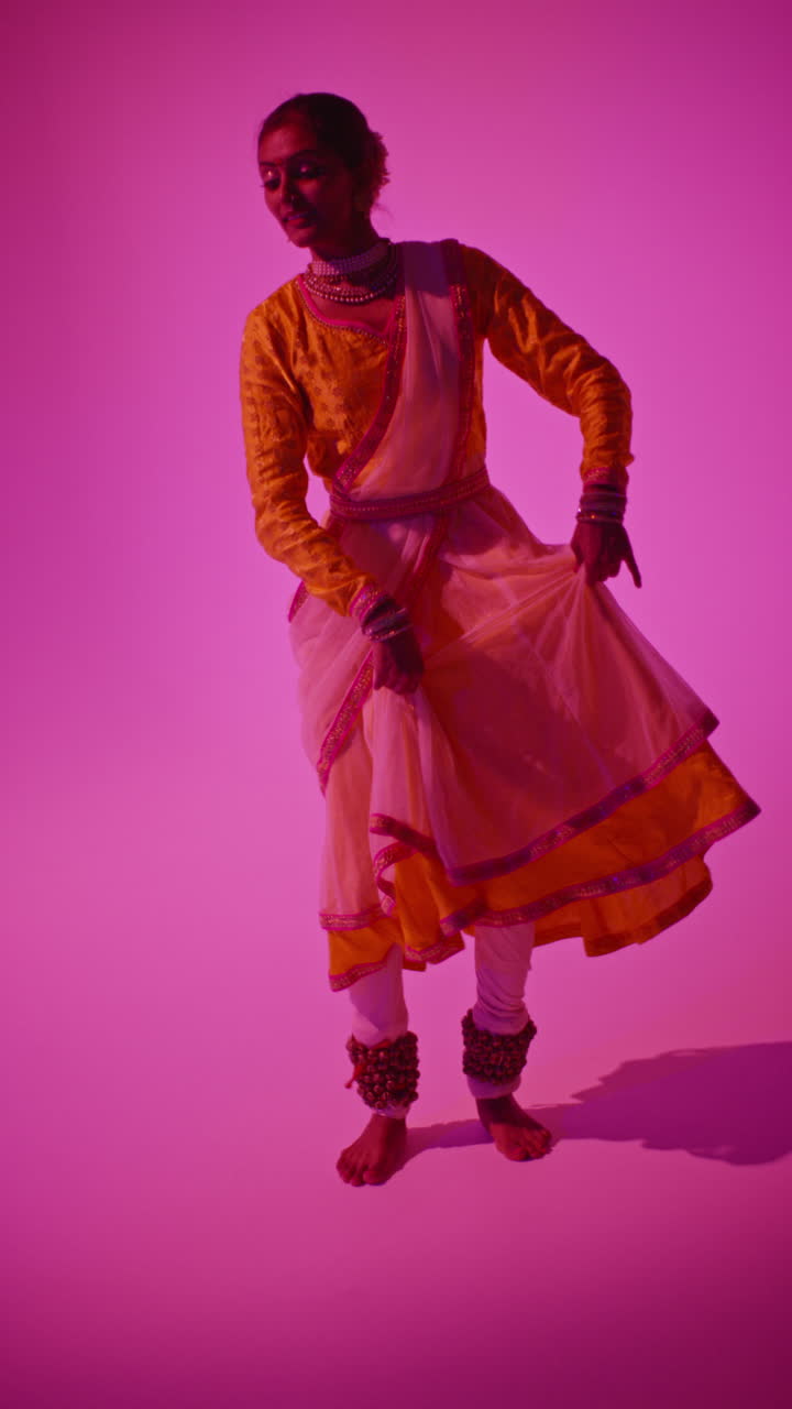 video vertical de larga duración en estudio de una bailarina de kathak que realiza un baile vestida con el vestido tradicional indio contra un fondo púrpura 4