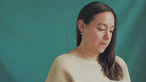 medium shot of a young woman in focus on a professional recording set, with a solid turquoise background