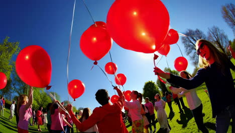 large group of people holding red balloons in a park