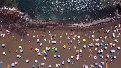 sunbathers relaxing on the beach under sun umbrellas at la arena beach of tenerife in the canary islands