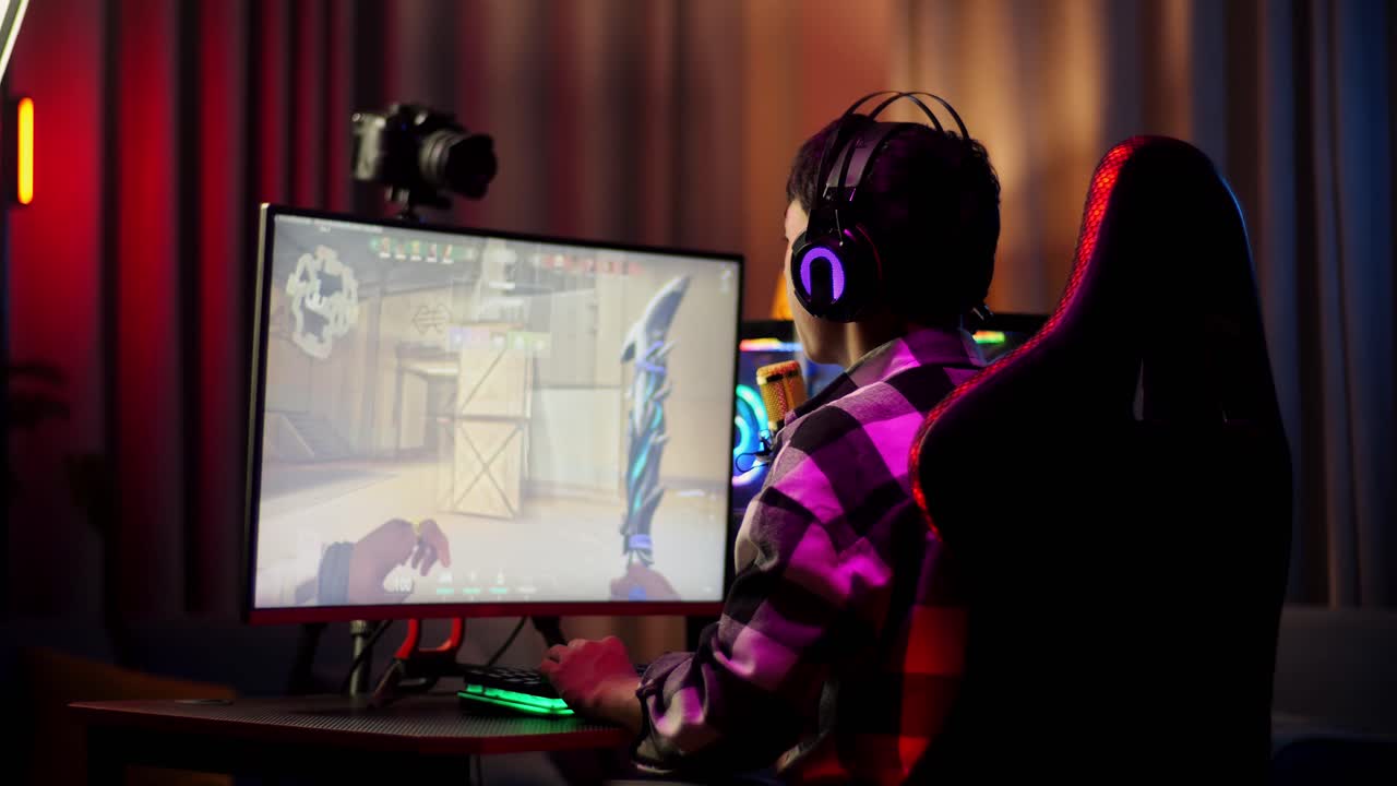 개인용 컴퓨터에서 네트워크를 통해 게임을 하는 아시아 소년 스트리머의 뒷면. 도전과 괴롭힘 경쟁자, 라이브 스트리밍 비디오 게임, rgb led 스트립 라이트에 의해 조명 된 책상