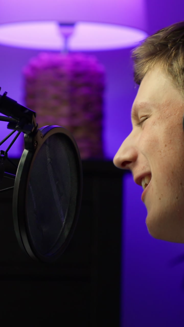 A teenage vocalist wearing headphones singing at the microphone in a recording studio, closeup vertical shot
