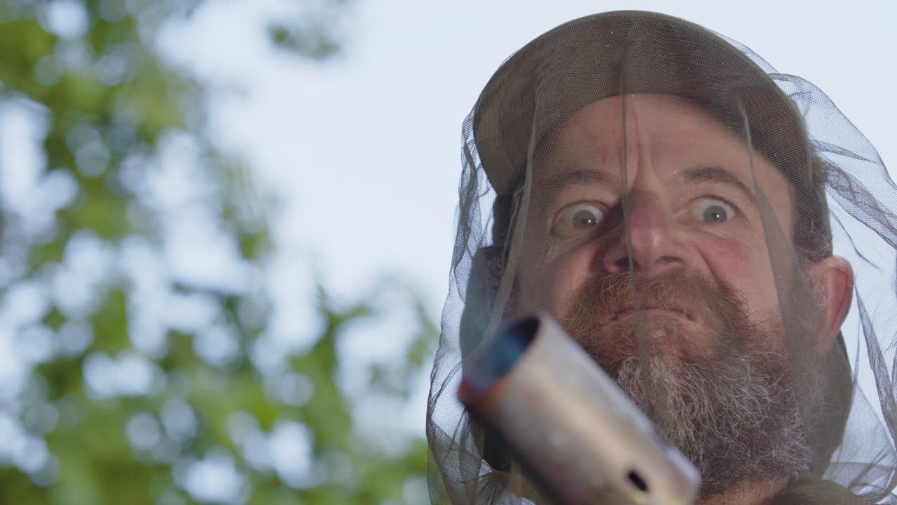 Bearded man with determined crazy eyes wearing mozzie head net lights blowtorch