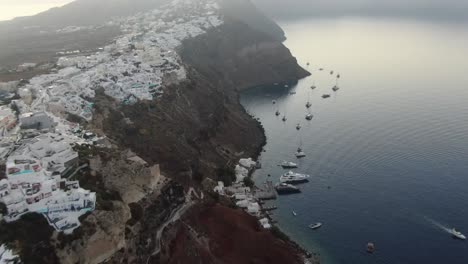 drone view in greece flying over santorini with oia town white houses on a cliff next to the mediterranean sea at sunrise