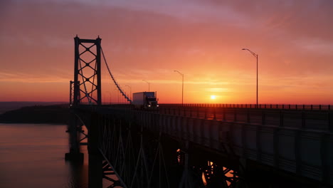 truck driving across a suspension bridge at sunset