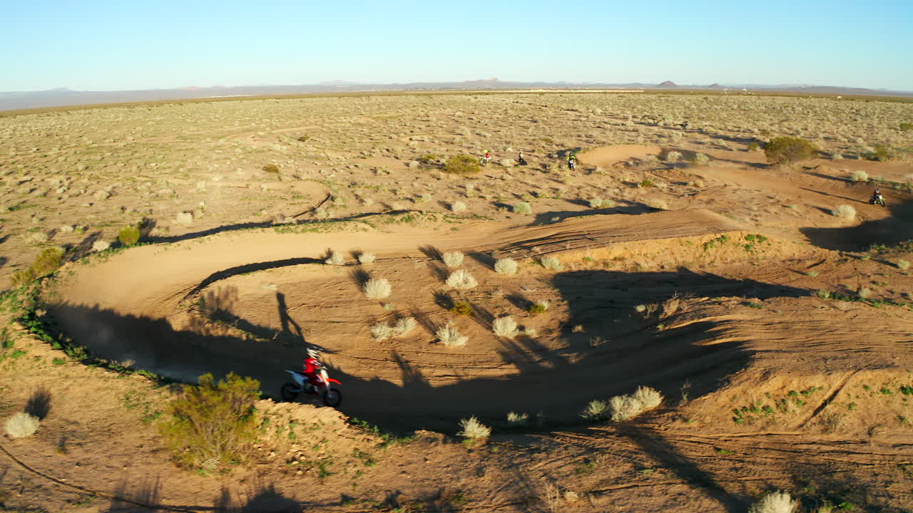 Motorcycle rider racing around a dusty dirt track in a goldern sandy desert