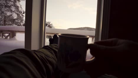 pov of a man drinking coffee on a couch inside the winter cottage