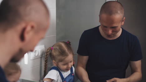 el hombre ensambla la maquinilla de afeitar mientras la hija pequeña se mira en el espejo