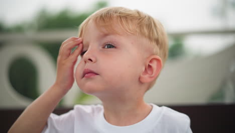 un niño curioso mira hacia arriba y hacia afuera con una expresión enfocada, mientras toca su cabeza