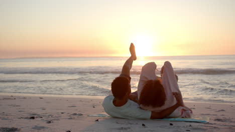 Una-Pareja-Birracial-Se-Relaja-En-La-Playa-Al-Atardecer,-Con-Las-Piernas-Levantadas-Juguetonamente-En-El-Aire-Con-Espacio-Para-Copiar