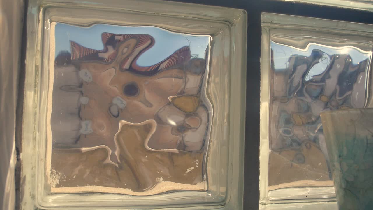 una toma lenta y elegante mirando por una ventana texturizada que distorsiona la vista de los edificios exteriores