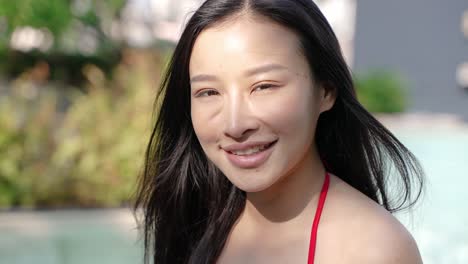 smiling asian woman in a red bikini by the pool