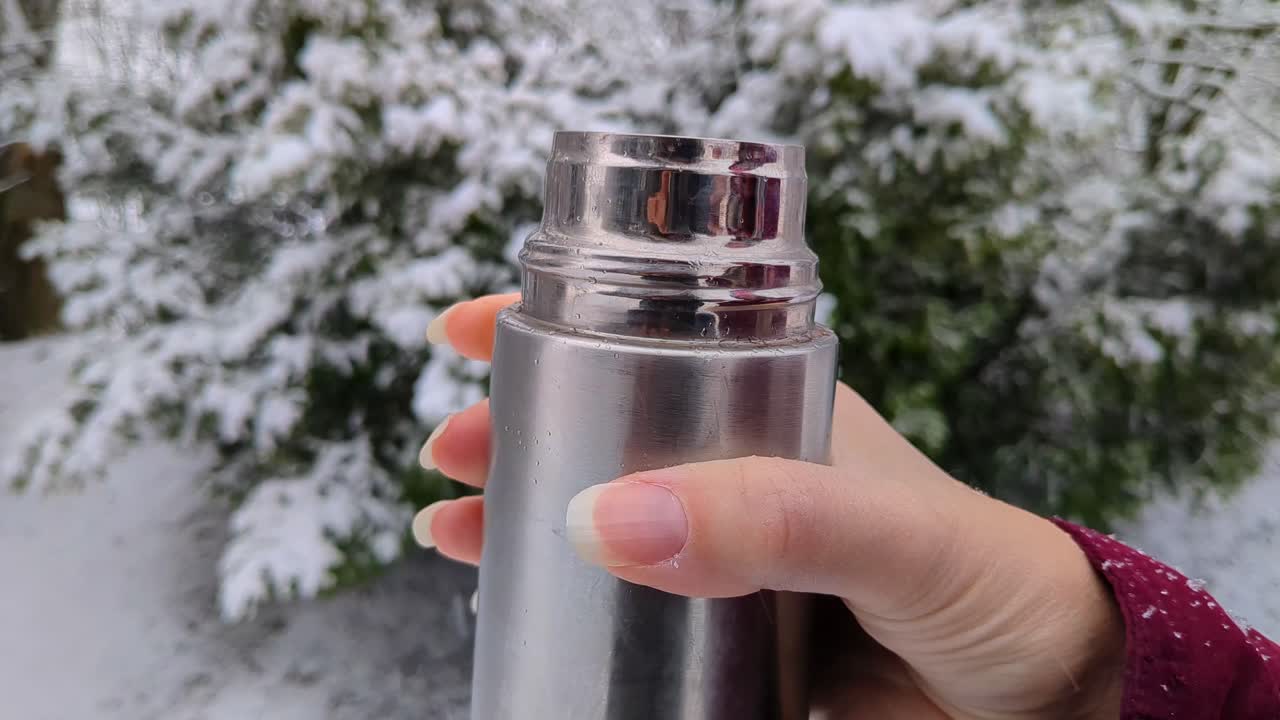 Woman drinking hot drink from thermos outside, snowing on winter day, close up
