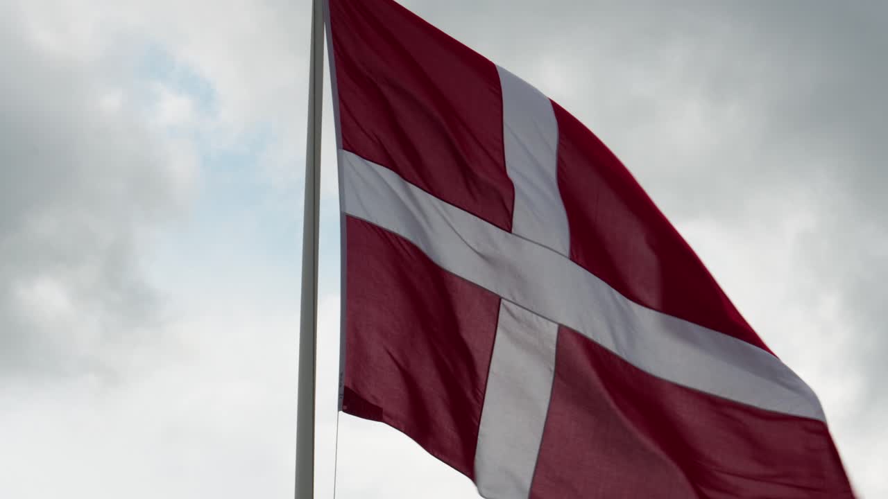 Flag of Denmark flying against a cloudy sky, with a focus on the flag waving