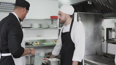 focused caucasian male chef instructing trainee male chef in kitchen, slow motion