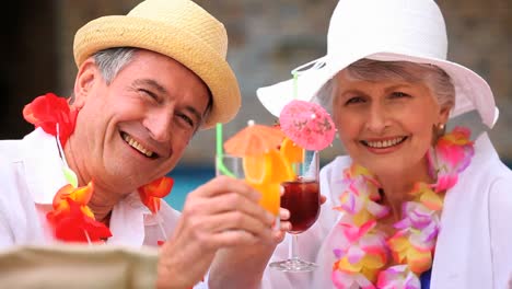 mature couple with hats and garlands drinking cocktails