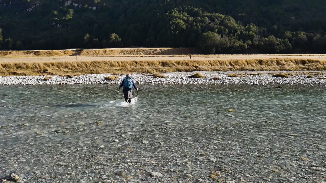 화창한 날 뉴질랜드에서 하이킹을 하며 흐르는 강을 건너는 배낭을 메고 있는 여성 - 후면 보기