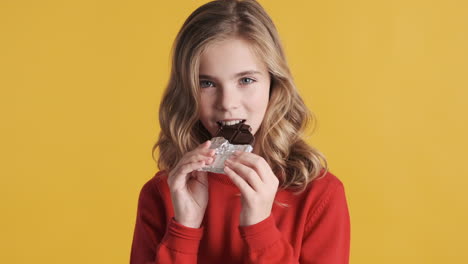 una adolescente caucásica comiendo una barra de chocolate.