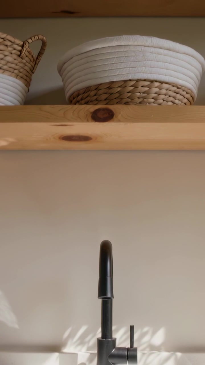 Vertical video: Panning camera revealing pine shelf above sink, showing black faucet and baskets