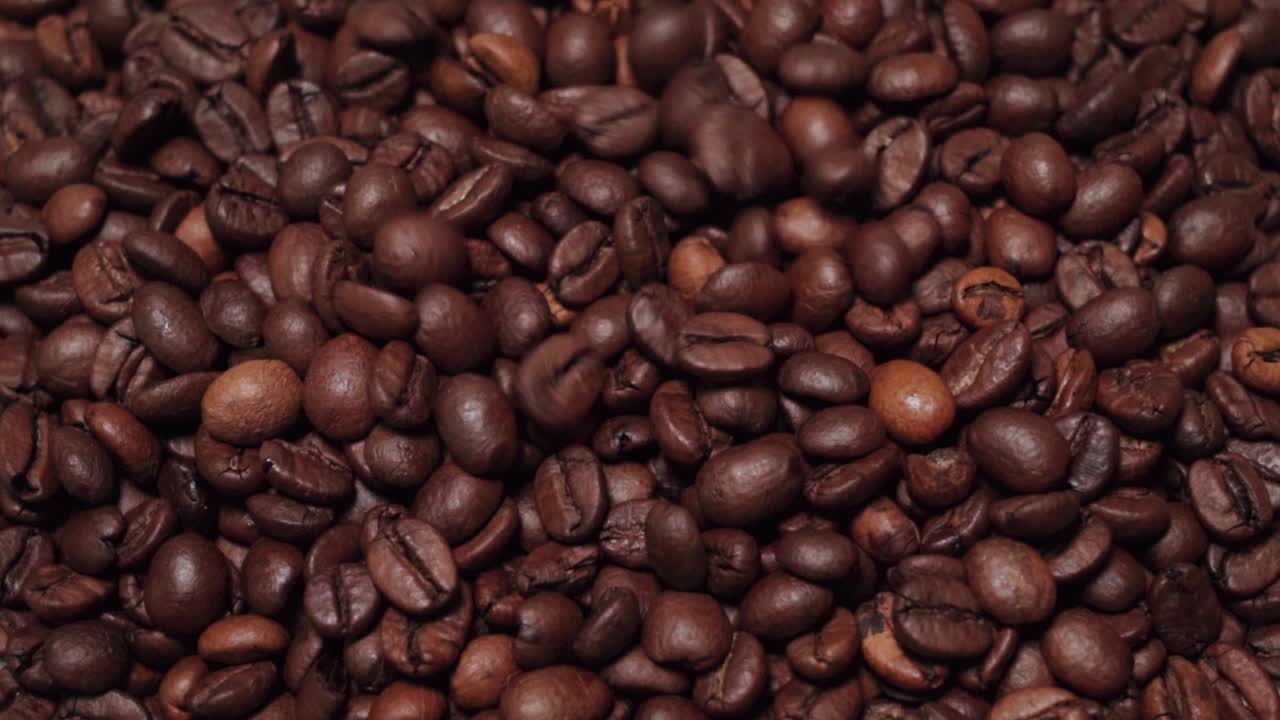 Dark roast coffee beans sprinkling onto solid background of beans, Slow Motion