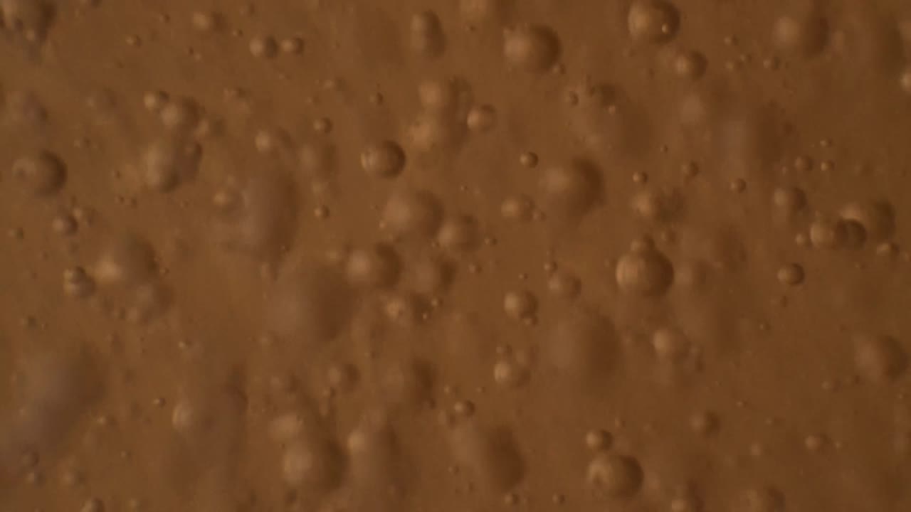 주황색 액체에 떠다니는 거품의 혼란스러운 움직임의 매크로 샷