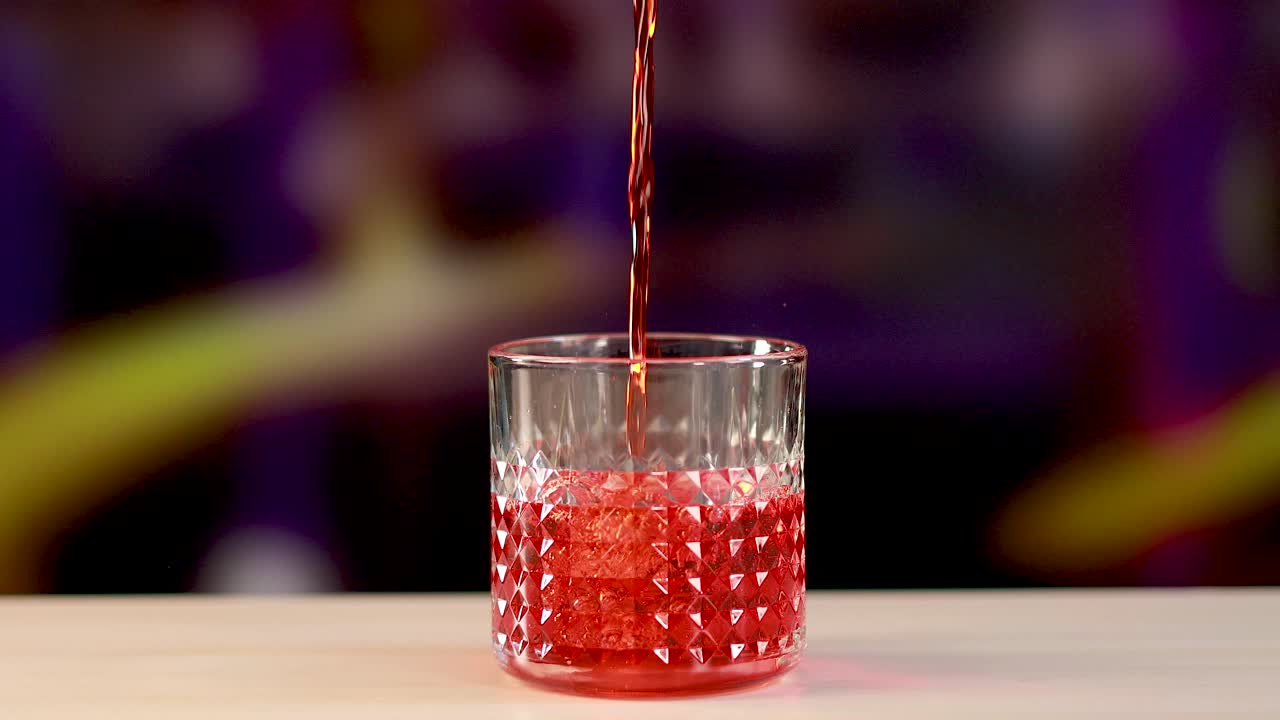 A vibrant Negroni cocktail is poured into a textured crystal glass against a colorful background, highlighting the drink's rich red hue