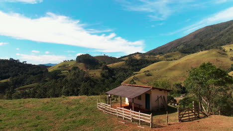 A-solitary-cottage-stands-amidst-rolling-green-hills-under-a-bright-blue-sky,-surrounded-by-nature