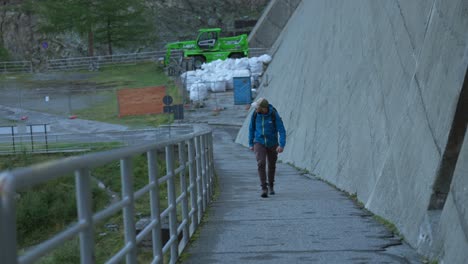 hombre caminando a lo largo de un camino de hormigón y una barandilla de metal