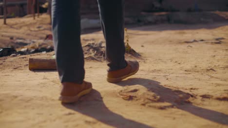young african man is walking slow on dirt road in local village towards house seeing only his legs, feet and shoes in ghana slowmotion 25 fps