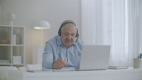 middle-aged man is communicating by online chat with colleagues and employees from home using laptop and headphones