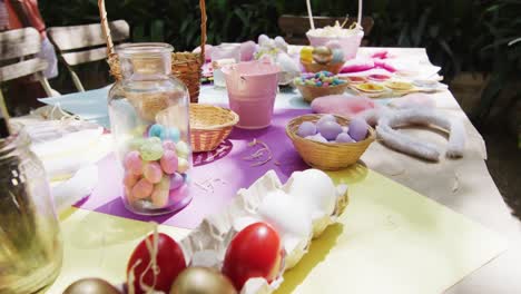 table in garden with bunny ears, baskets, painted and sugar eggs for easter celebration, slow motion