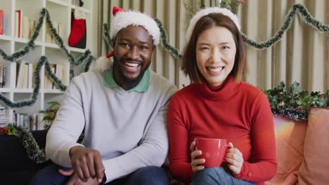 video of happy diverse couple in santa hats making christmas video call at home holding gifts