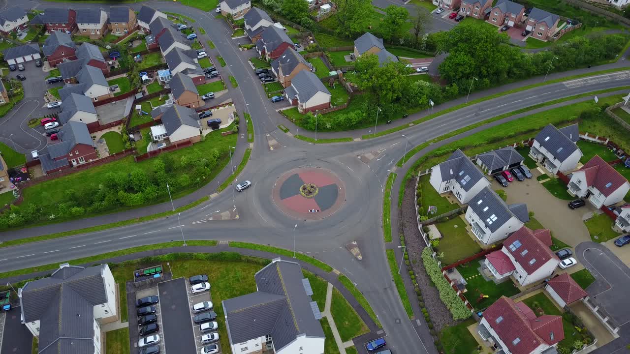 Aerial video of a roundabout through cars circulate surrounded by buildings and some vegetation