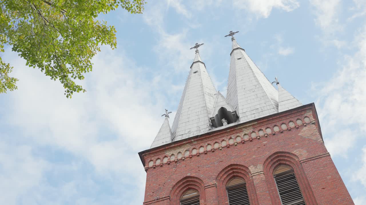 Una vista dal basso cattura i campanili gemelli di una storica chiesa in mattoni contro un cielo luminoso e parzialmente nuvoloso. Perfetto per progetti a tema architettonico o religioso.