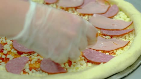 cook prepares pizza with bacon and smoked sausage adds slices of bacon