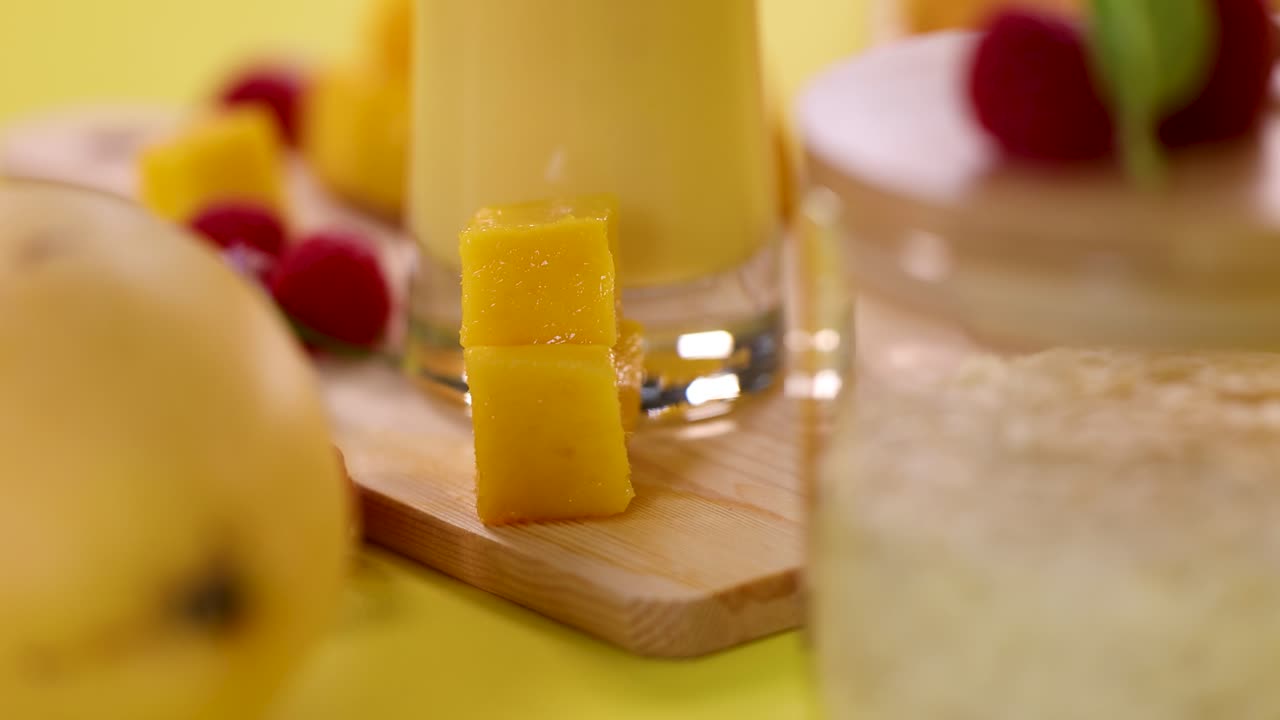 Close-up of mango smoothie, fruit cubes, raspberries, and rice on a vibrant yellow surface
