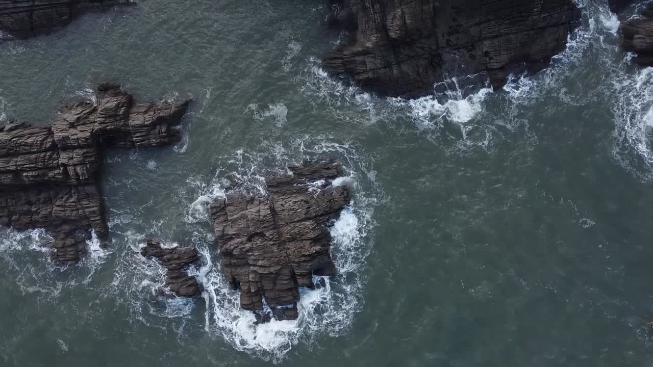 Vista aerea con drone a volo d'uccello di persone su un paddleboard multiposto blu che navigano tra le rocce lungo la costa sotto una scogliera rocciosa - Lee Bay, Beach, Ilfracombe, Devon, Inghilterra