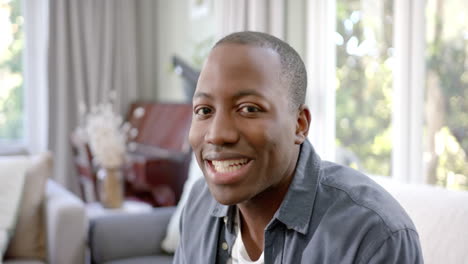 Portrait-of-happy-african-american-man-sitting-in-sunny-living-room-smiling,-slow-motion