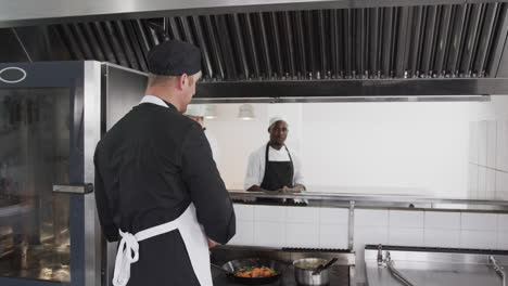 focused diverse male chef instructing trainee male chefs in kitchen, slow motion