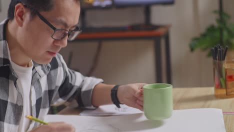 close up of asian male drinking coffee while working on a car design sketch on table in the studio