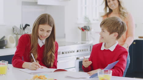 Madre-Ayudando-A-Niños-En-Uniforme-Escolar-Haciendo-Los-Deberes-En-La-Cocina