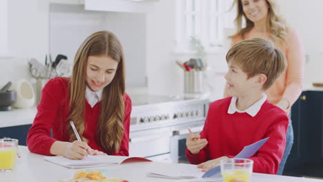 mother helping children in school uniform doing homework at kitchen counter