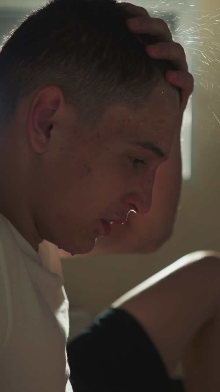 atleta hombre agotado frota el cabello mojado con la mano sentado en el suelo en el club para deportes de lucha. descanso después de movimientos activos. sudor goteando de la frente y sentirse cansado después del entrenamiento